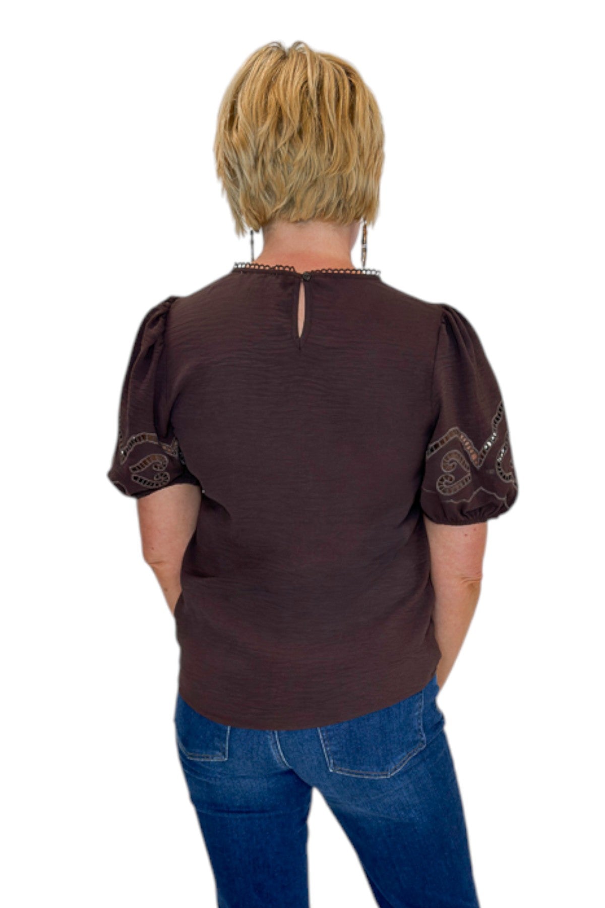 Back view of woman wearing Swagger Boutique’s Brown Embroidered Short Sleeve Top with jeans against white studio background.