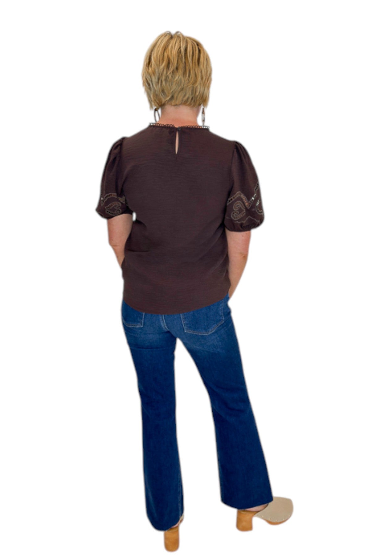Back view of woman wearing Swagger Boutique’s Brown Embroidered Short Sleeve Top with jeans against white studio background.