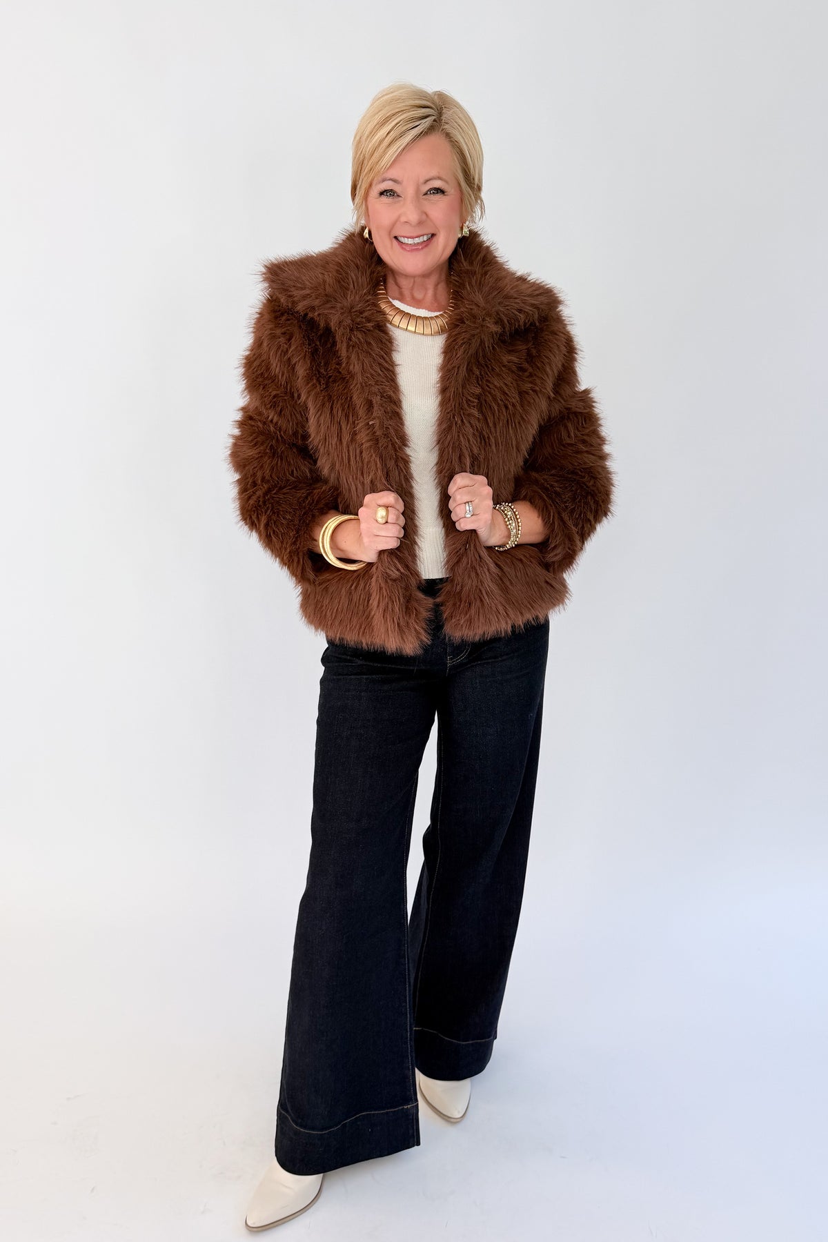 Front view of woman wearing Swagger Boutique’s Brown Faux Fur Jacket with jeans against white studio background.