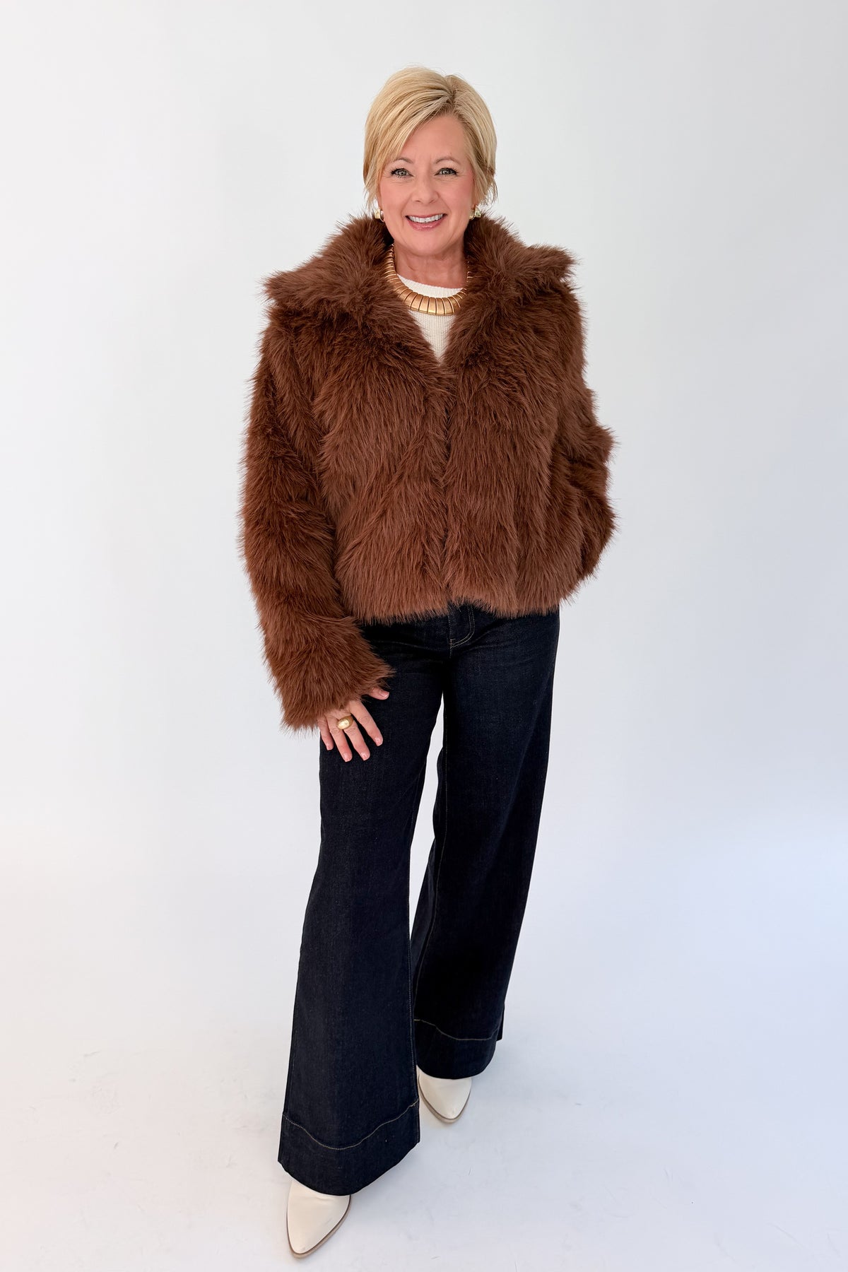 Front view of woman wearing Swagger Boutique’s Brown Faux Fur Jacket with jeans against white studio background.