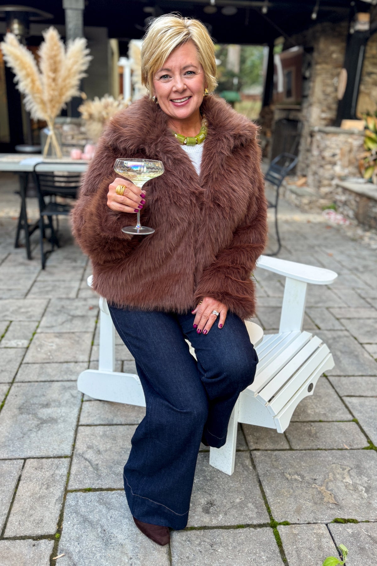 Front view of woman wearing Swagger Boutique’s Brown Faux Fur Jacket with jeans sitting outside at a party.