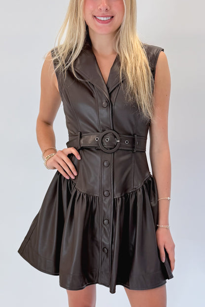 Front detail view of woman wearing Swagger Boutique’s Brown Faux Leather Mini Dress with heels against white studio background.