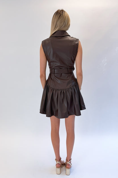 Back view of woman wearing Swagger Boutique’s Brown Faux Leather Mini Dress with heels against white studio background.