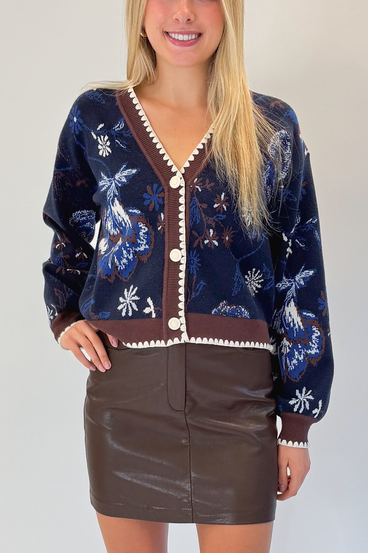 Front detail view of woman wearing Swagger Boutique’s Navy &amp; Brown Printed Cardigan with Brown Faux Leather Mini Skirt against white studio background.