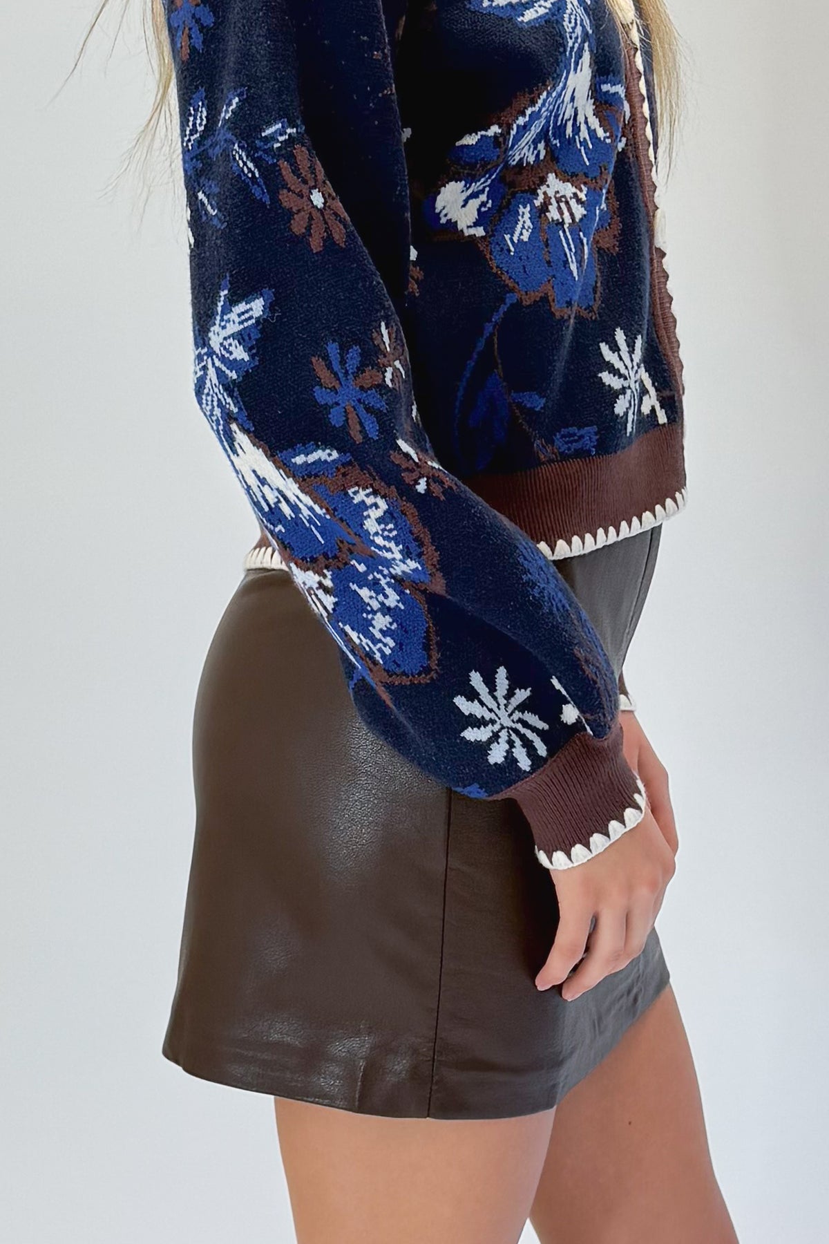 Side detail view of woman wearing Swagger Boutique’s Navy &amp; Brown Printed Cardigan with Brown Faux Leather Mini Skirt against white studio background.