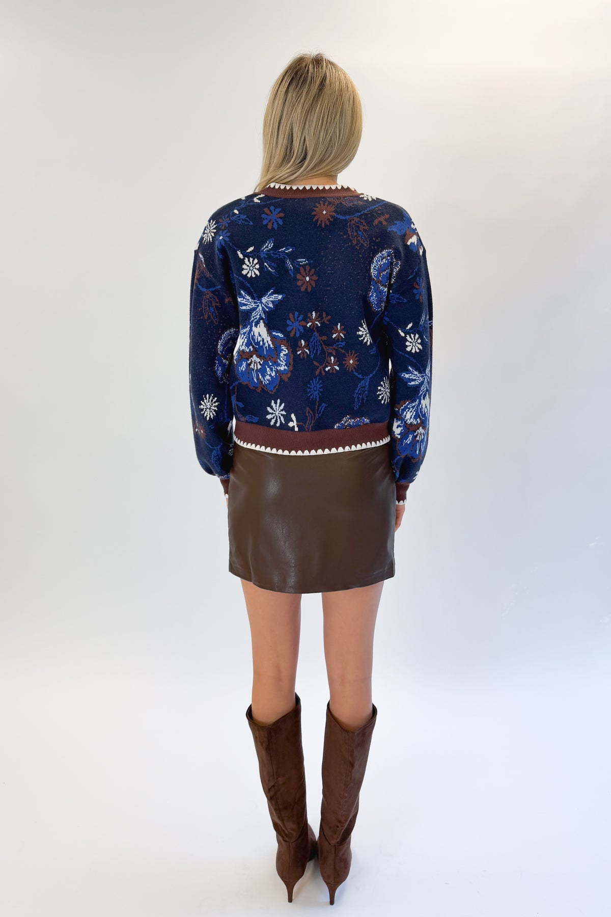 Back view of woman wearing Swagger Boutique’s Navy &amp; Brown Printed Cardigan with Brown Faux Leather Mini Skirt against white studio background.