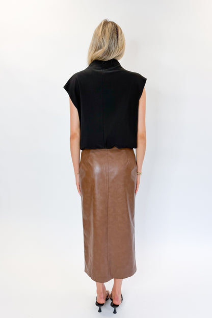 Back view of woman wearing Swagger Boutique’s Brown Faux Leather Slit Midi Skirt with black top against white studio background.
