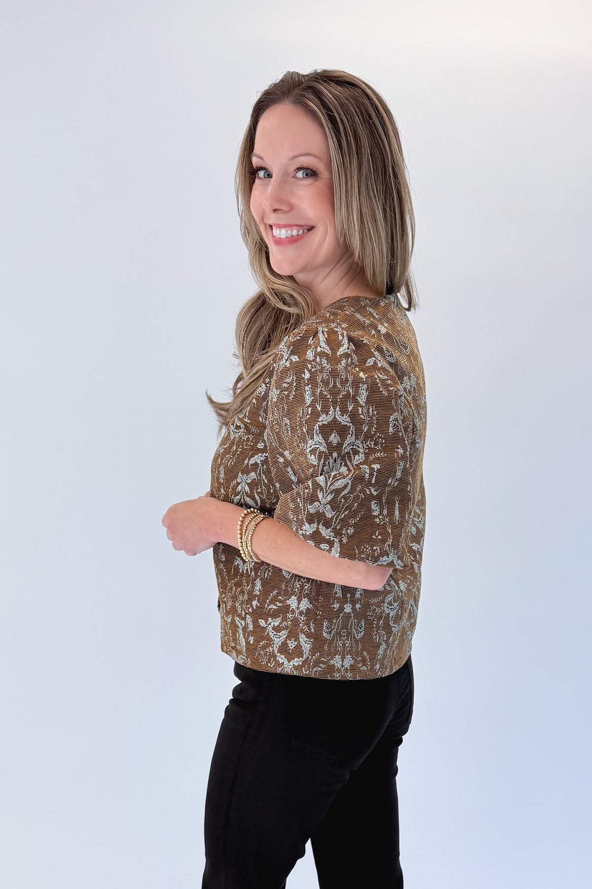 Side view of woman wearing Swagger Boutique’s Brown Floral Corduroy Top with jeans against white studio background.
