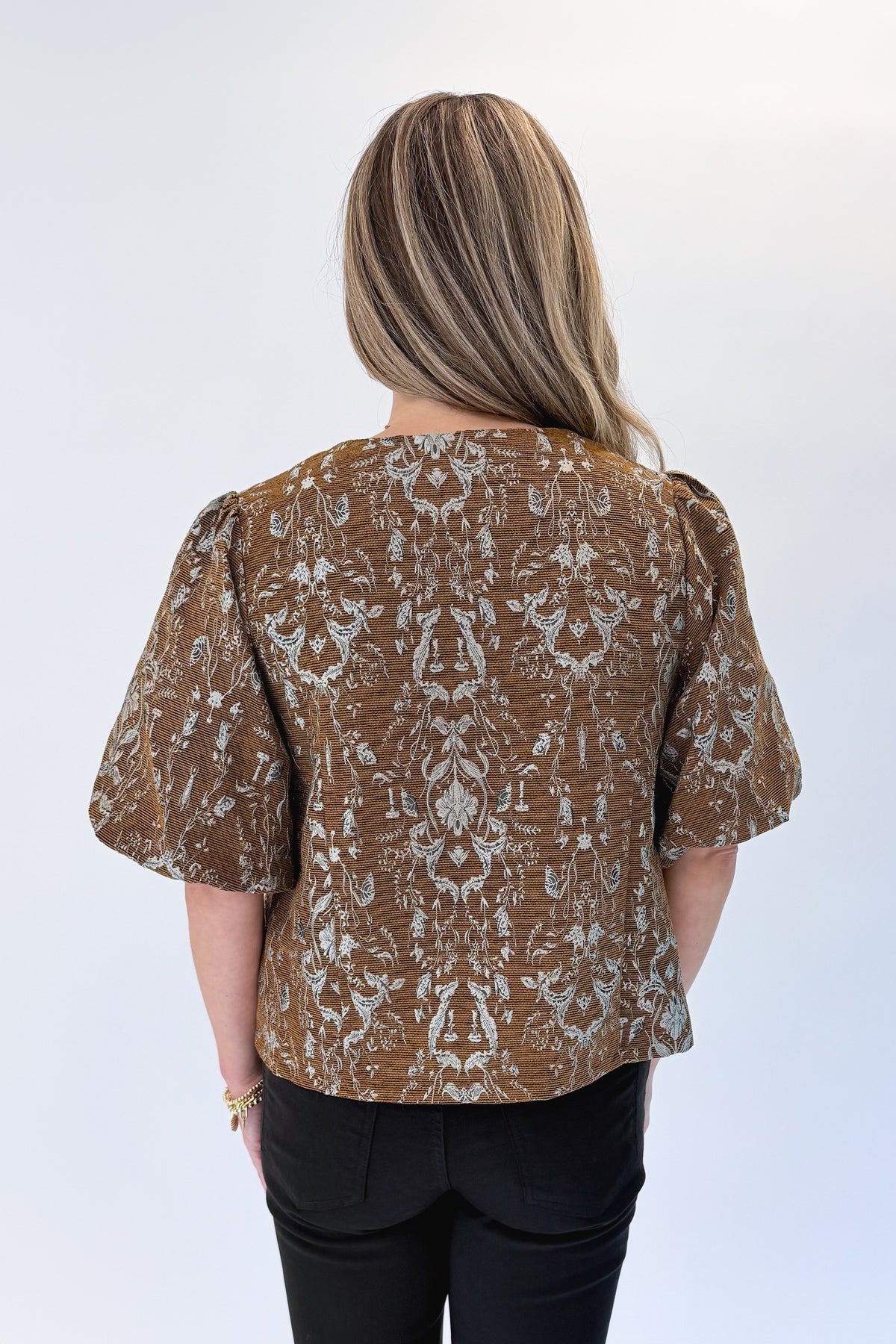 Back view of woman wearing Swagger Boutique’s Brown Floral Corduroy Top with jeans against white studio background.