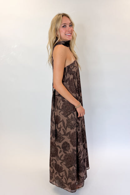 Side view of woman wearing Swagger Boutique’s Brown Floral Strapless Maxi Dress with heels against white studio background.