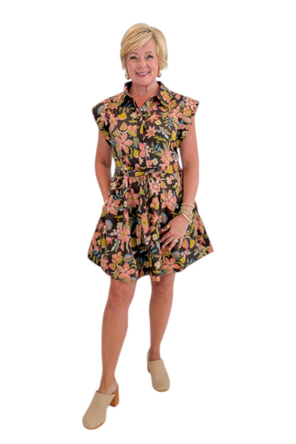 Front view of woman wearing Swagger Boutique’s Brown Floral Tie Waist Mini Dress by Entro with clogs against white studio background.