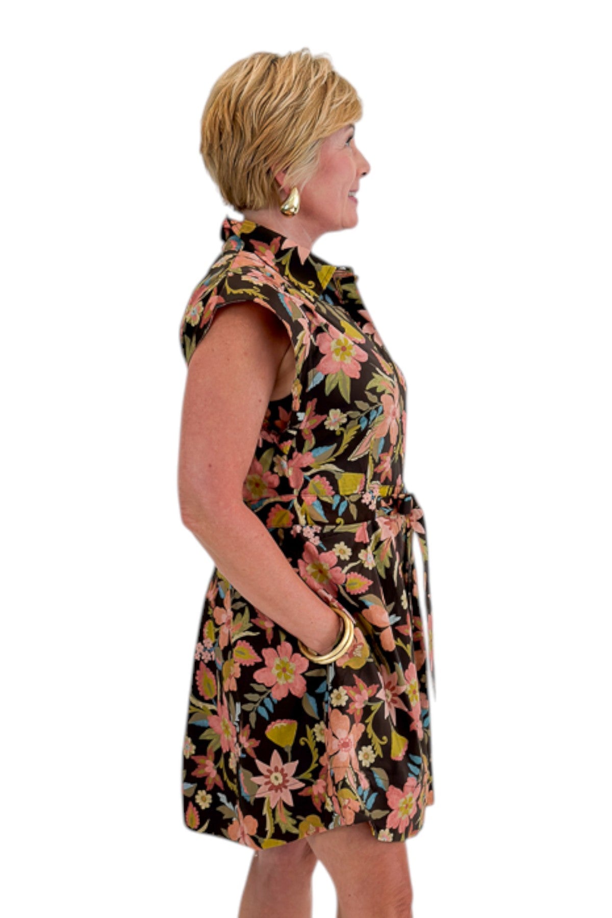 Side view of woman wearing Swagger Boutique’s Brown Floral Tie Waist Mini Dress by Entro with clogs against white studio background.