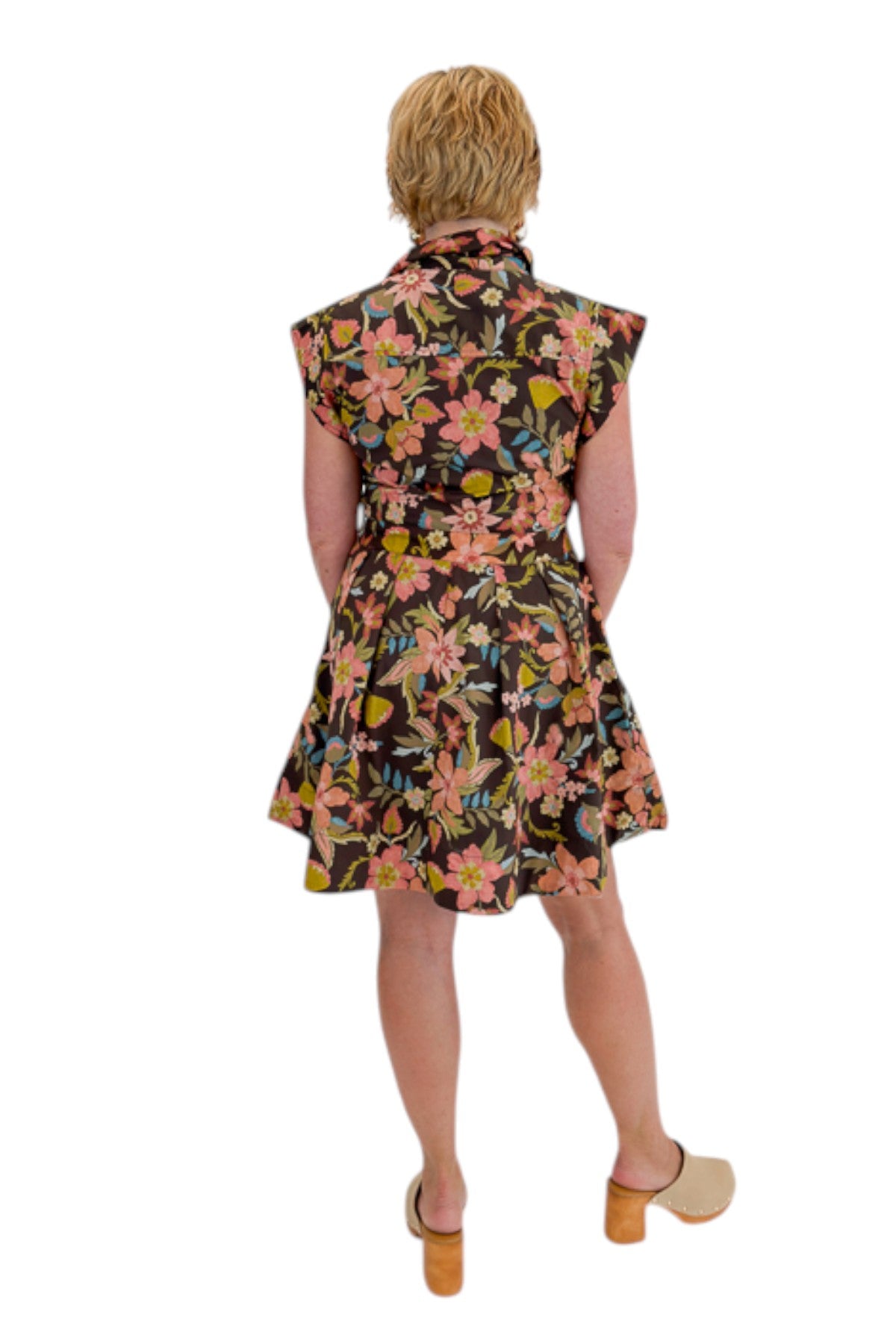 Back view of woman wearing Swagger Boutique’s Brown Floral Tie Waist Mini Dress by Entro with clogs against white studio background.