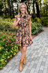 Front view of woman wearing Swagger Boutique’s Brown Floral Tie Waist Mini Dress by Entro with boots walking down a path outside. 
