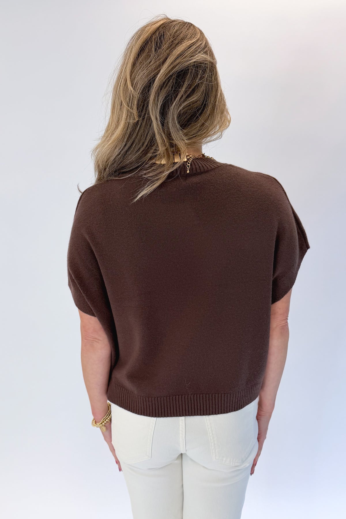 Back view of woman wearing Swagger Boutique’s Brown Light Weight Short Sleeve Sweater with jeans against white studio background.