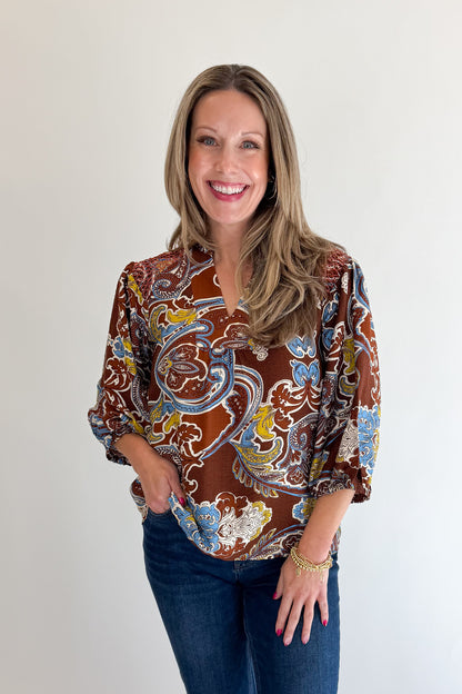 Front view of woman wearing Swagger Boutique’s Brown Paisley Print V-Neck Top with jeans against white studio background.