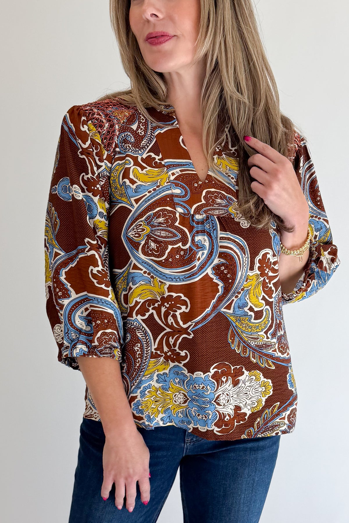 Front detail view of woman wearing Swagger Boutique’s Brown Paisley Print V-Neck Top with jeans against white studio background.