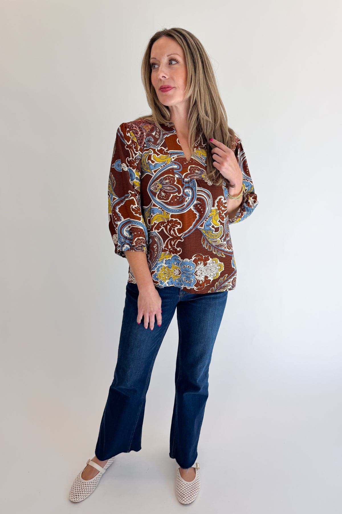 Front view of woman wearing Swagger Boutique’s Brown Paisley Print V-Neck Top with jeans against white studio background.