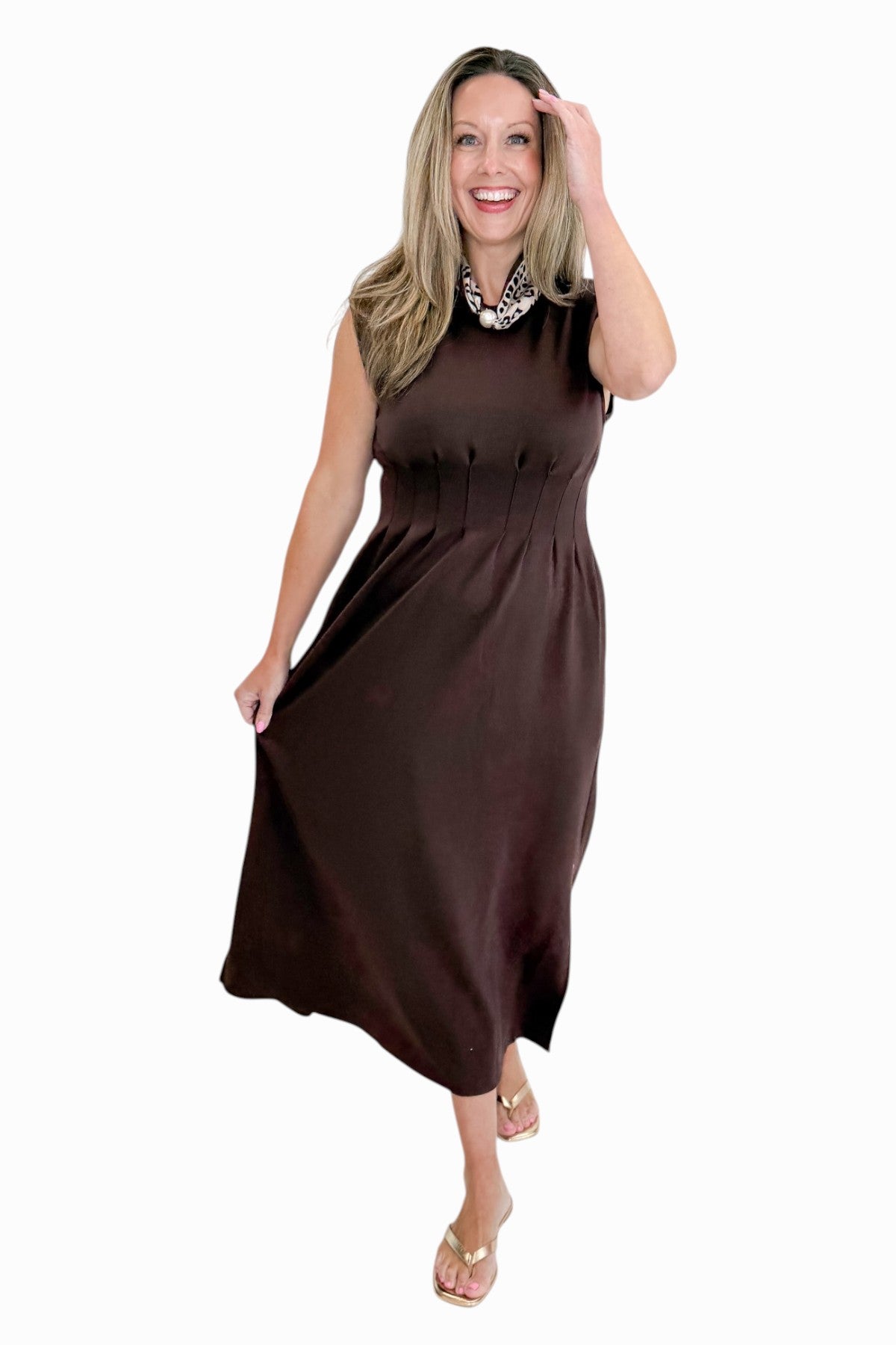 Front view of woman wearing Swagger Boutique’s Brown Pintuck Waist Midi Dress by Entro with sandals against white studio background.