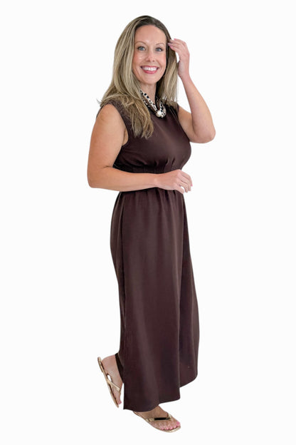 Side view of woman wearing Swagger Boutique’s Brown Pintuck Waist Midi Dress by Entro with sandals against white studio background.