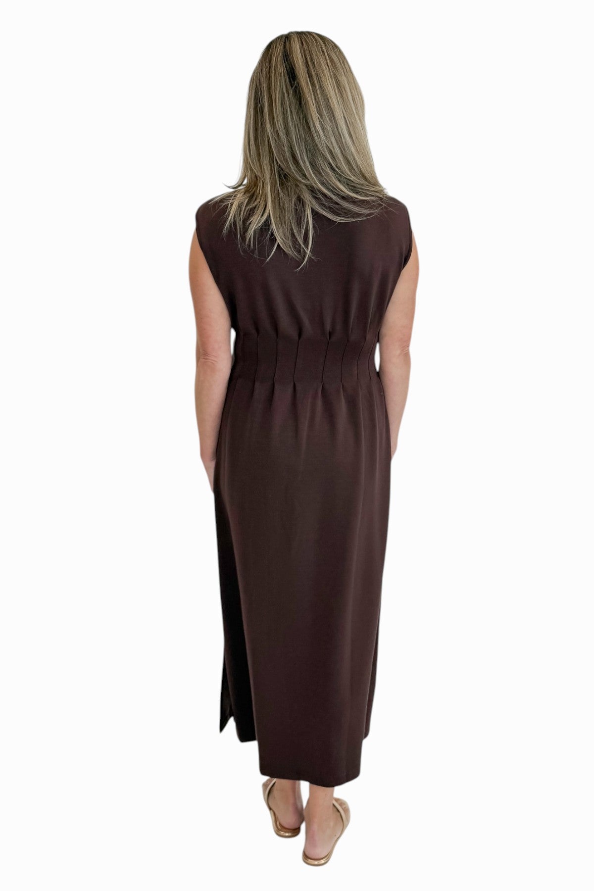 Back view of woman wearing Swagger Boutique’s Brown Pintuck Waist Midi Dress by Entro with sandals against white studio background.