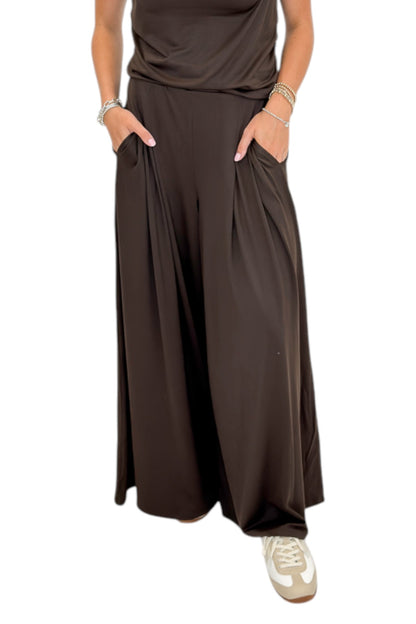 Front detail view of woman wearing Swagger Boutique’s Brown Pleated Wide Leg Pants with Brown Rouched Side Tank against white studio background.