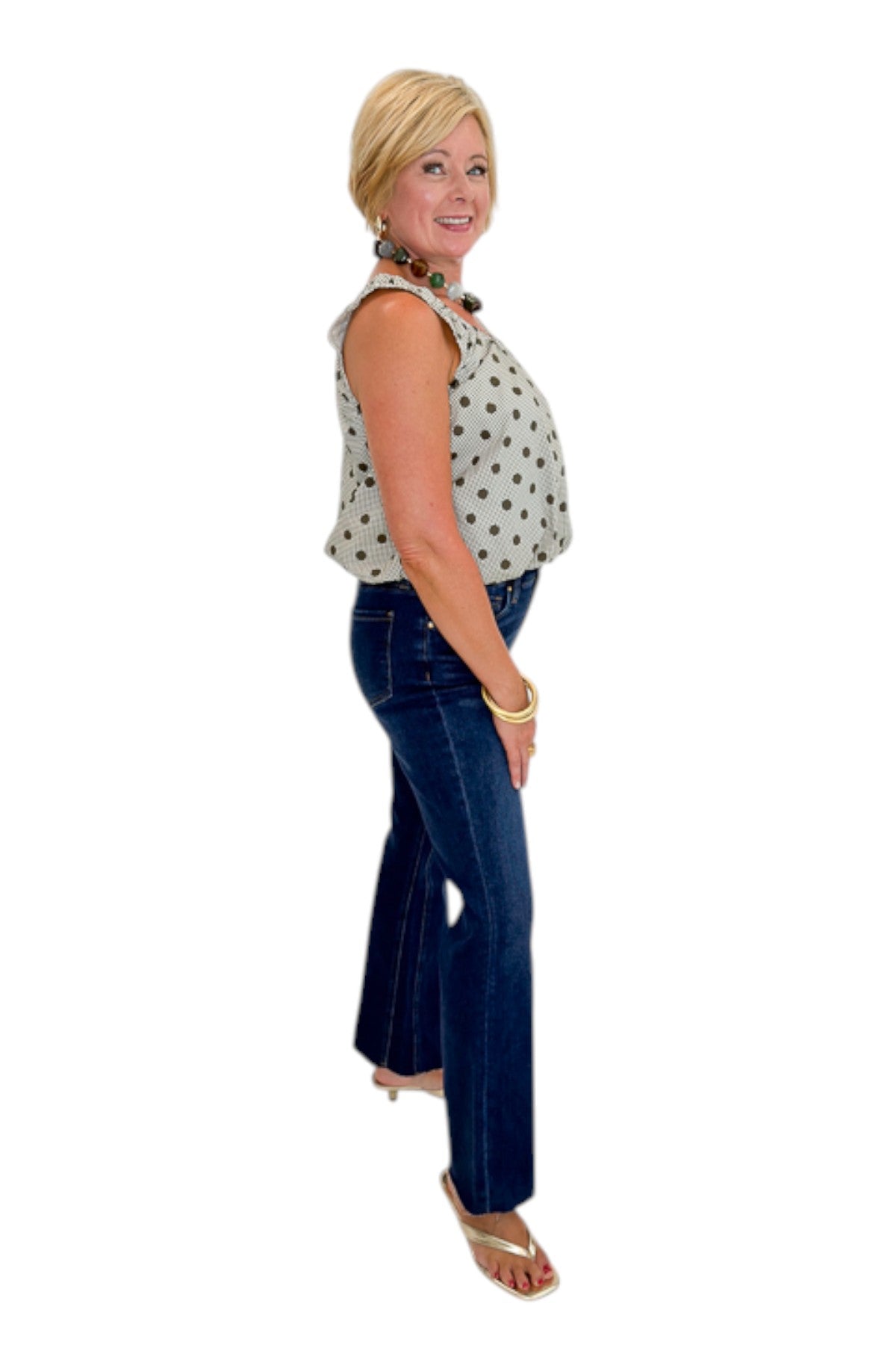 Side view of woman wearing Swagger Boutique’s Brown Polka Dot Bubble Hem Tank with jeans against white studio background.