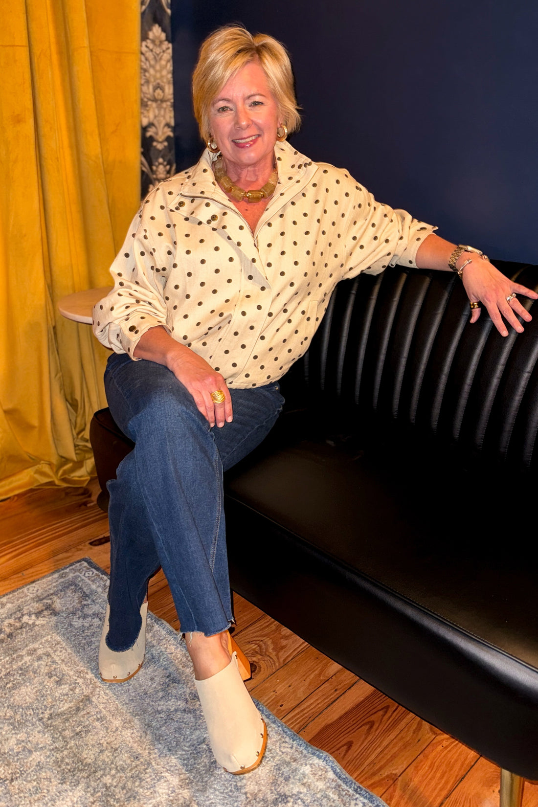 Front view of woman wearing Swagger Boutique’s Brown Polka Dot Denim Jacket with jeans sitting on a couch.