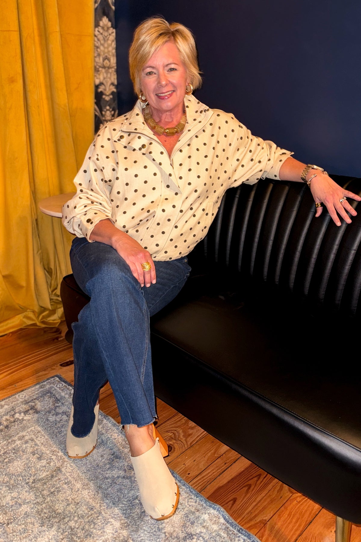 Front view of woman wearing Swagger Boutique’s Brown Polka Dot Denim Jacket with jeans sitting on a couch.