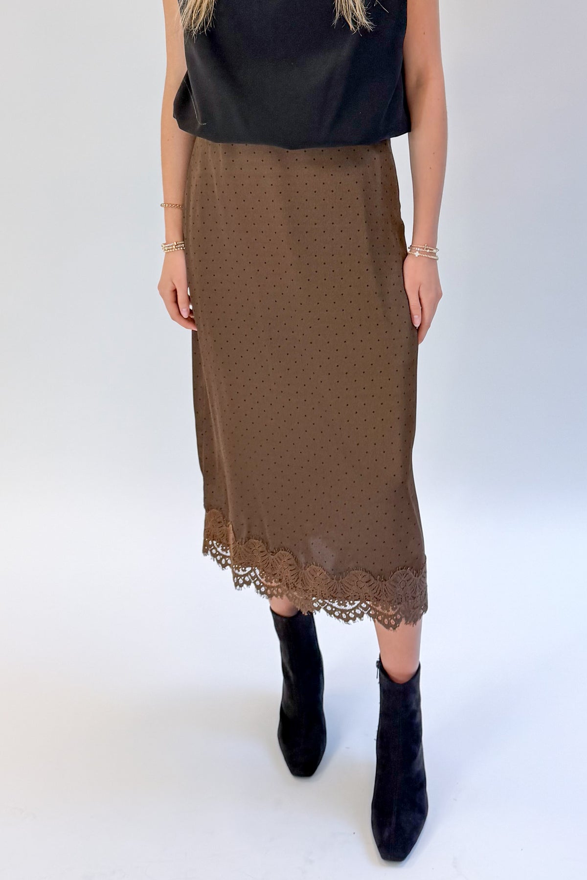 Front detail view of woman wearing Swagger Boutique’s Brown Polka Dot Lace Lined Satin Skirt by Entro with Black Satin Cowlneck Sleeveless Top against white studio background.