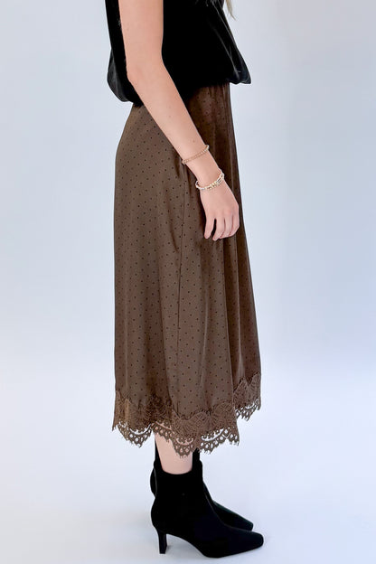 Side detail view of woman wearing Swagger Boutique’s Brown Polka Dot Lace Lined Satin Skirt by Entro with Black Satin Cowlneck Sleeveless Top against white studio background.