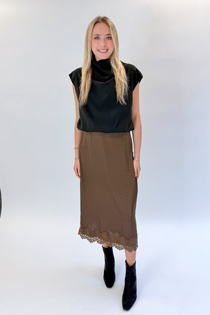 Front view of woman wearing Swagger Boutique’s Brown Polka Dot Lace Lined Satin Skirt by Entro with Black Satin Cowlneck Sleeveless Top against white studio background.