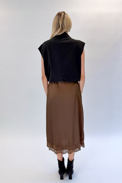 Back view of woman wearing Swagger Boutique’s Brown Polka Dot Lace Lined Satin Skirt by Entro with Black Satin Cowlneck Sleeveless Top against white studio background.
