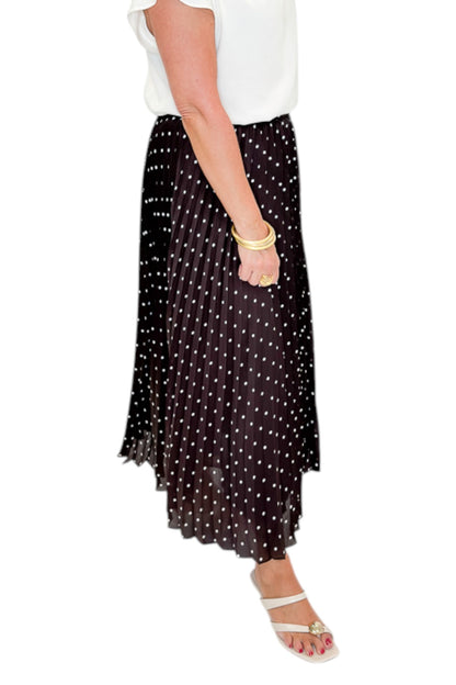 Side detail view of woman wearing Swagger Boutique’s Brown Polka Dot Pleated Skirt with top against white studio background.
