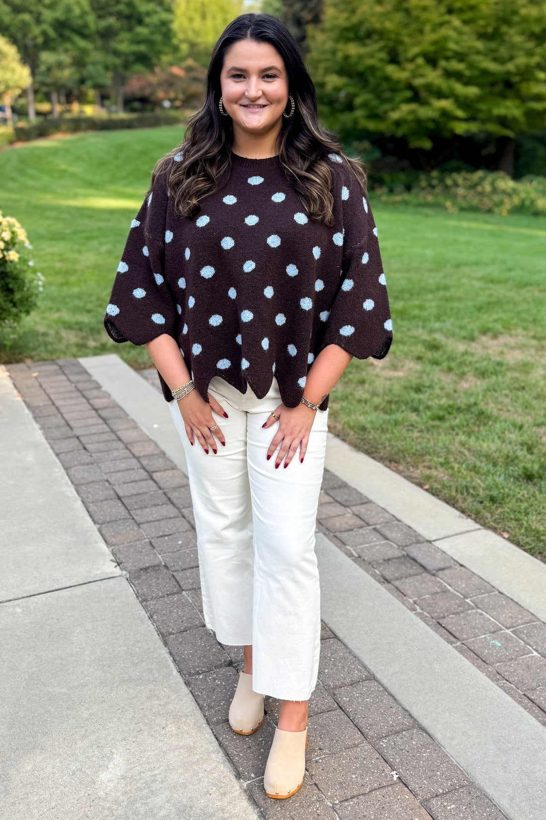 Front view of woman wearing Swagger Boutique’s Brown Polka Dot Short Sleeve Sweater by Entro with jeans standing outside on a brick walkway.