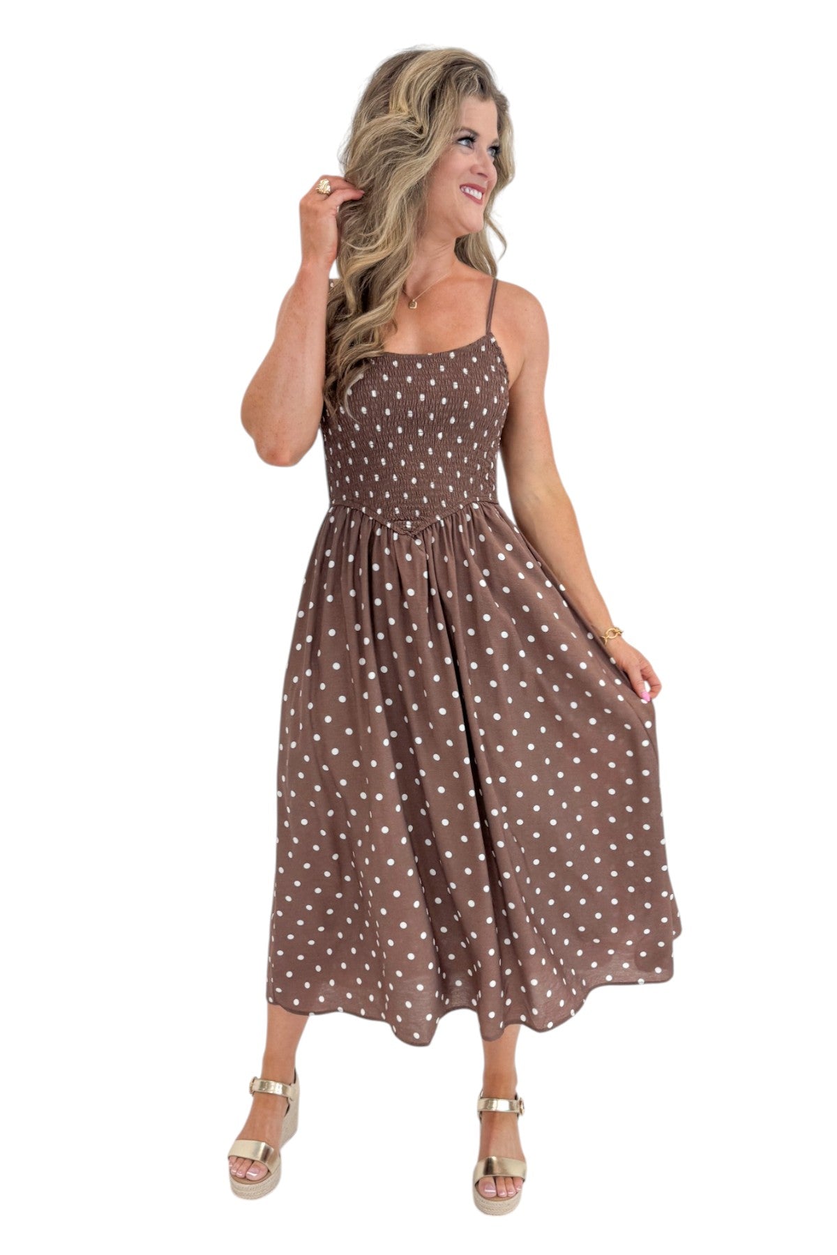 Front view of woman wearing Swagger Boutique’s Brown Polka Dot Smocked Midi Dress with sandals against white studio background.