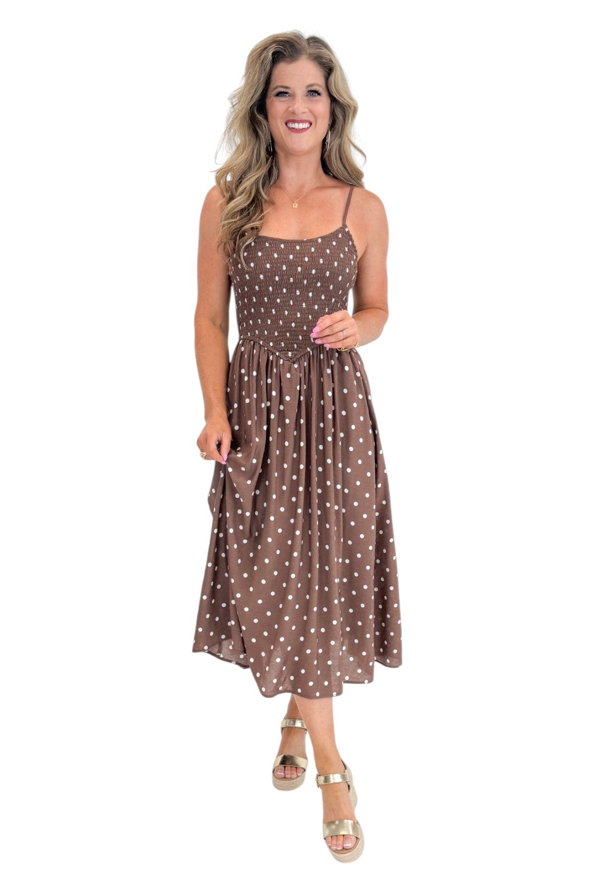 Front view of woman wearing Swagger Boutique’s Brown Polka Dot Smocked Midi Dress with sandals against white studio background.