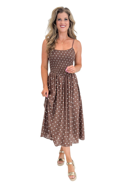 Front view of woman wearing Swagger Boutique’s Brown Polka Dot Smocked Midi Dress with sandals against white studio background.