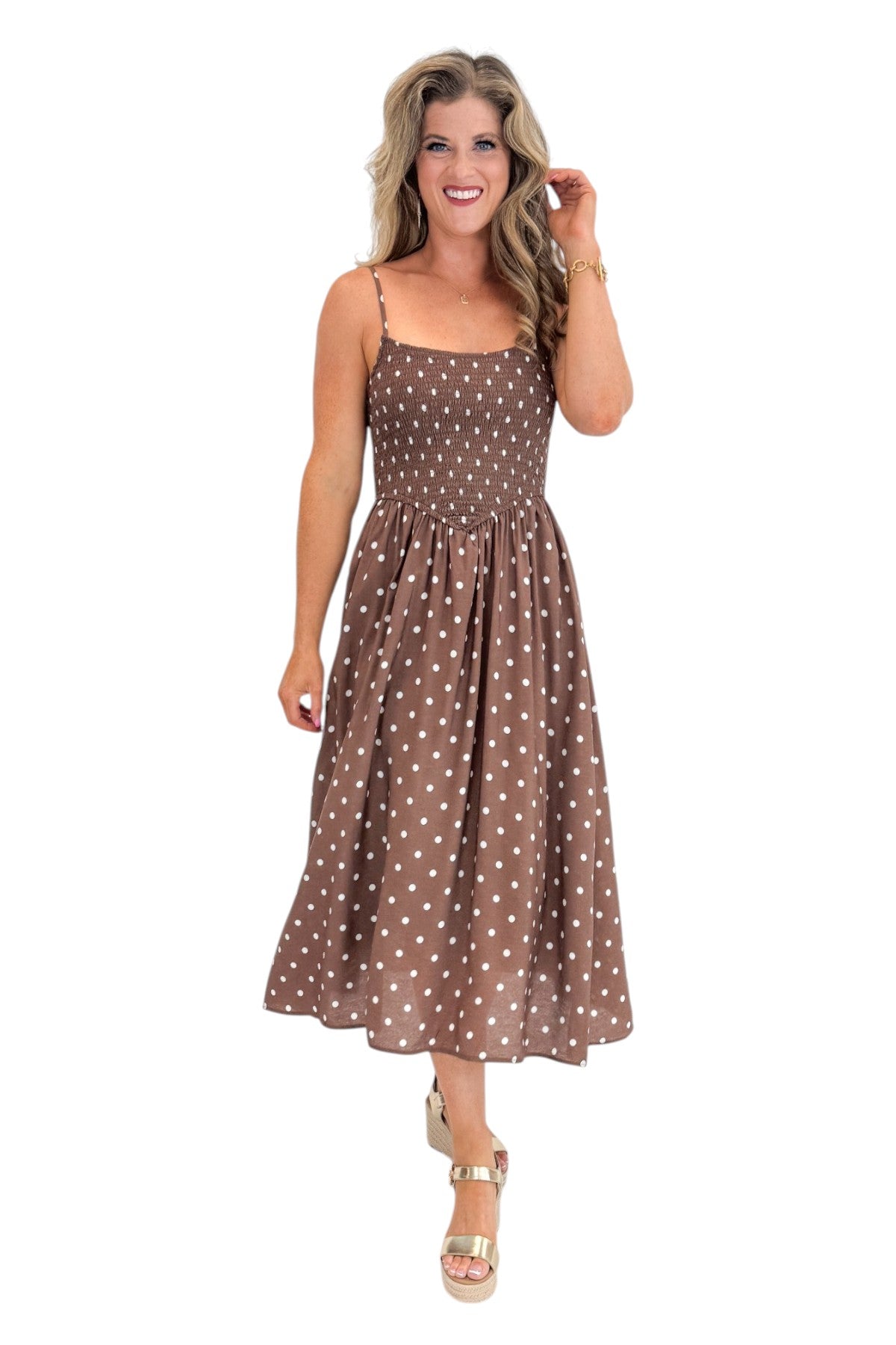 Front view of woman wearing Swagger Boutique’s Brown Polka Dot Smocked Midi Dress with sandals against white studio background.