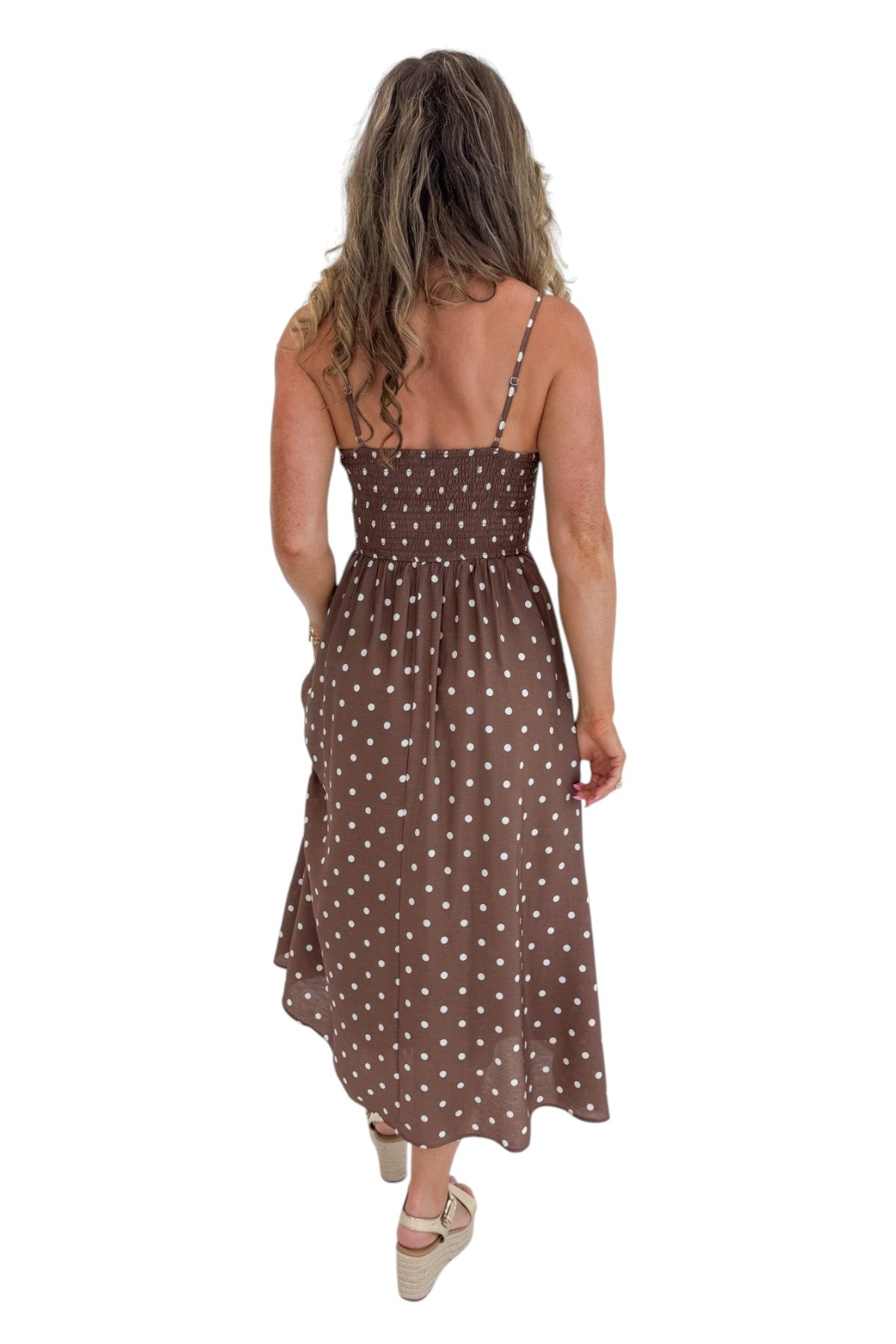 Back view of woman wearing Swagger Boutique’s Brown Polka Dot Smocked Midi Dress with sandals against white studio background.