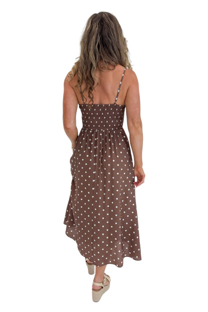 Back view of woman wearing Swagger Boutique’s Brown Polka Dot Smocked Midi Dress with sandals against white studio background.