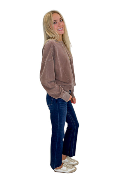 Side view of woman wearing Swagger Boutique’s Brown Ribbed Detail Sweatshirt with jeans against white studio background.