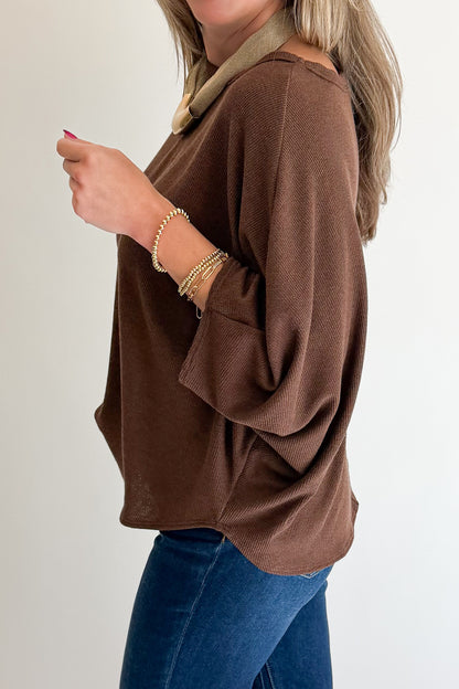 A woman wearing a brown knit long-sleeve top with a beige collar, paired with blue jeans, shown from the side against a plain light background.