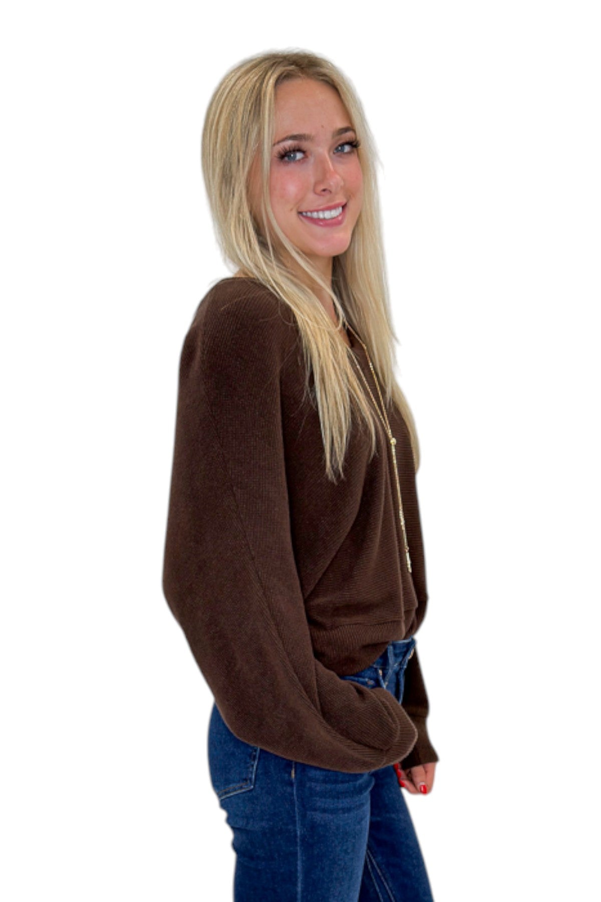 Side view of woman wearing Swagger Boutique’s Brown Ribbed V-neck Banded Top with jeans against white studio background.