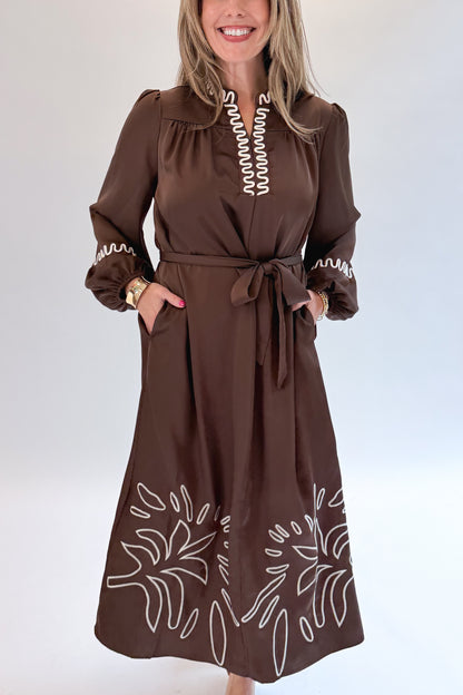 Front detail view of woman wearing Swagger Boutique’s Brown Satin Embroidered Midi Dress with heels against white studio background.