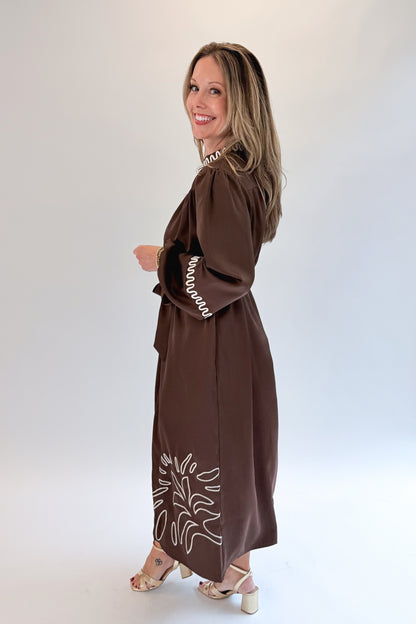 Side view of woman wearing Swagger Boutique’s Brown Satin Embroidered Midi Dress with heels against white studio background.