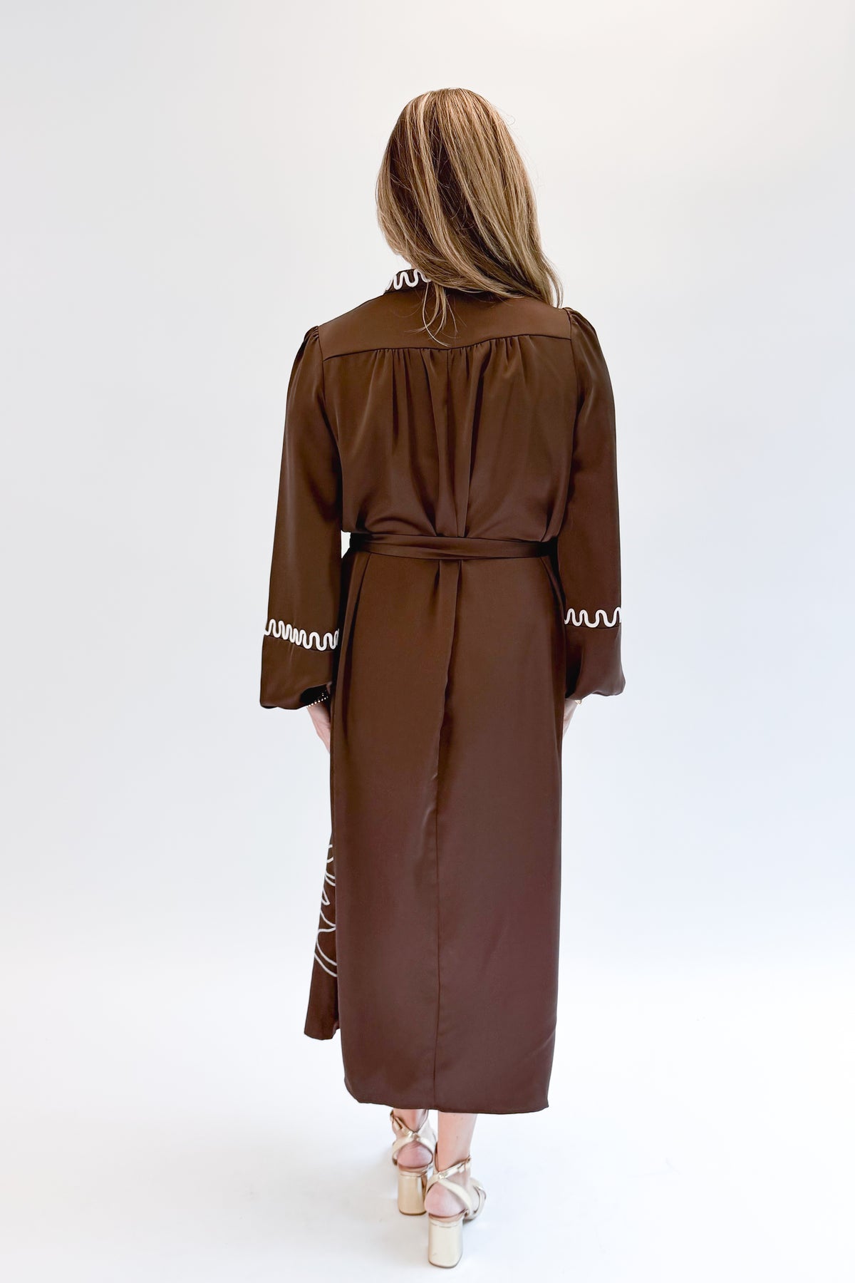 Back view of woman wearing Swagger Boutique’s Brown Satin Embroidered Midi Dress with heels against white studio background.