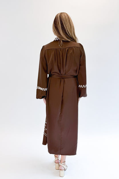 Back view of woman wearing Swagger Boutique’s Brown Satin Embroidered Midi Dress with heels against white studio background.