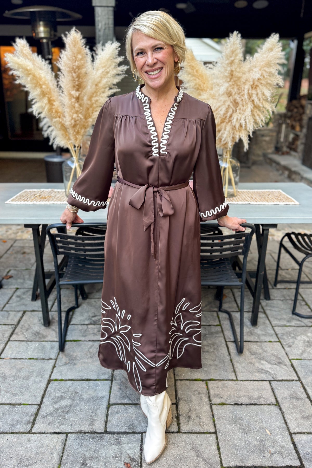 Front view of woman wearing Swagger Boutique’s Brown Satin Embroidered Midi Dress standing outside at a party.