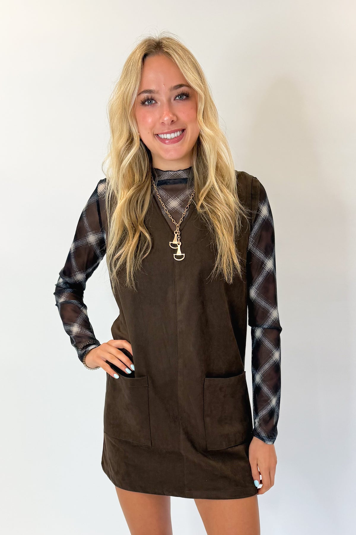 Front view of woman wearing Swagger Boutique’s Brown Suede V-Neck Mini Dress with Navy Plaid Mesh Top against white studio background.